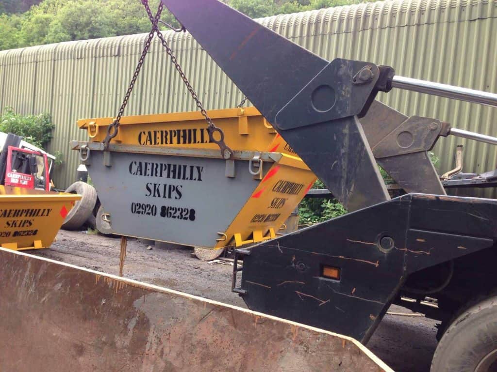 Skip hire service in Newport in progress with yellow mini skip being taken from a road